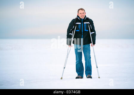 Man with crutches walking outdoors on winter day Stock Photo