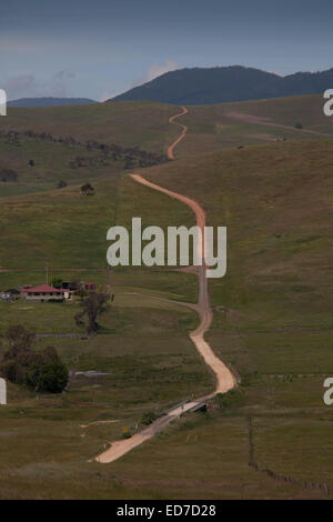 Dirt road leading past a red roofed farmhouse in Alpine Region of Victoria Australia Stock Photo