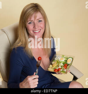 Woman in a blue dress eating takeaway cold food.  An egg and tomato salad healthy eating Stock Photo