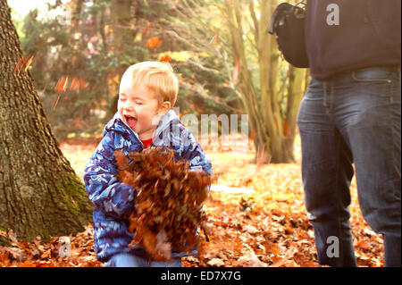 Boy laughing throwing leaves around in autumn in the park Stock Photo