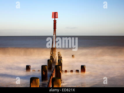 A creative image of a breakwater with marker post in a moderate sea at Cart Gap, Norfolk, England, United Kingdom. Stock Photo