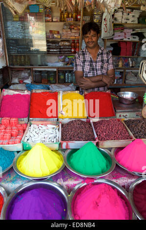 MYSORE, INDIA - NOVEMBER 4, 2012: Young Indian vendor stands behind colorful piles of bindi powder in the Devaraja market. Stock Photo