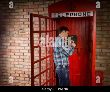Man standing making a call in a red British telephone booth with a vintage dial-up instrument Stock Photo
