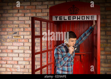 Man chatting inside a red British telephone booth leaning in the open doorway listening to the conversation Stock Photo