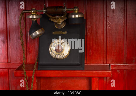 Old retro vintage rotary dial-up telephone instrument with a handset and cradle mounted on a red wooden wall Stock Photo