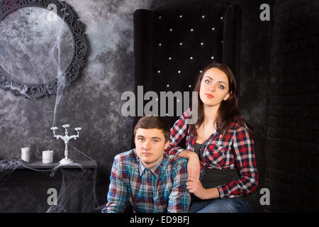 Close Up of Young Couple Wearing Plaid Shirts Sitting in Black High Back Chair in Haunted House Setting Stock Photo