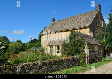 A Cotswold stone English cottage with a garden full of flowers and a British flag in Upper Slaughter, Cotswolds, UK. Stock Photo