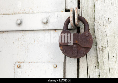 Big old rusted padlock hanging on white door Stock Photo