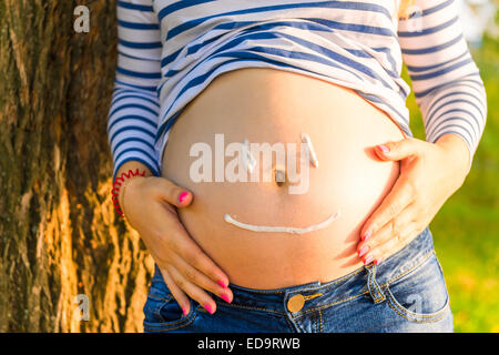 on the belly of a pregnant woman painted cheerful smiley Stock Photo