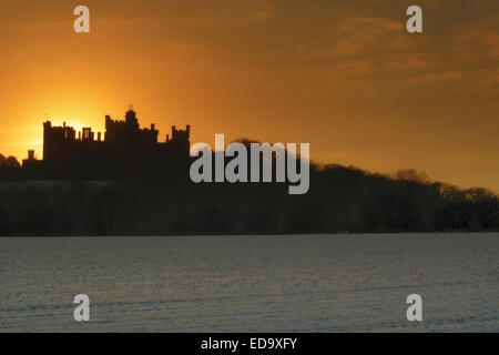 Belvoir Castle silhouetted against a winter sunset. The field in the foreground is  covered in snow. Stock Photo