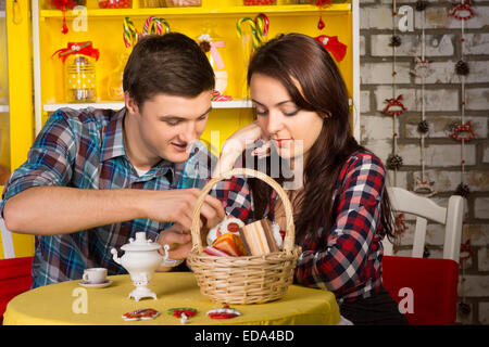 Sweet Young Lovers in Checkered Shirts Dating at the Shop with Pastry Basket and Drinks on the Table. Stock Photo