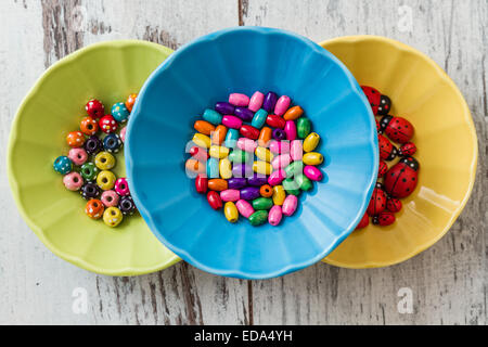 Multi colored beads in colorful dishes on white wooden table Stock Photo