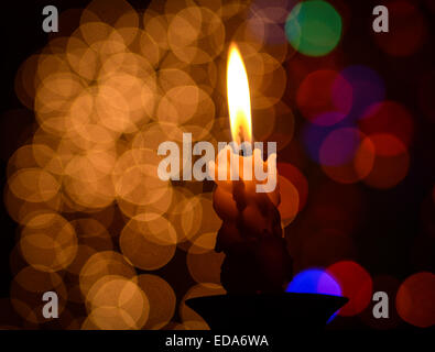 A lit candle in front of soft focus Christmas lights Stock Photo