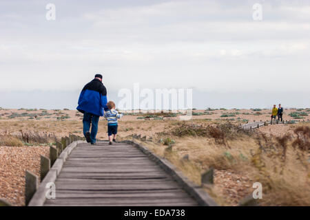 Father and son walk down to the beach on the wooden boardwalk at Dungeness, Kent, England Stock Photo