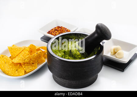 Pestle and Mortar filled with avocado and chili pepper garlic for making Guacamole, accompanied by corn tortilla chips Stock Photo