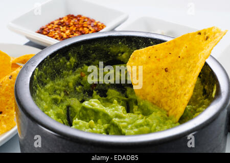 Pestle and Mortar filled with avocado and chili pepper spices for making Guacamole, accompanied by corn tortilla chips Stock Photo
