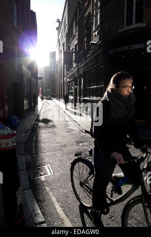 A young woman cycles along Sandy's Row on a sunny winter morning in Spitalfields East London KATHY DEWITT Stock Photo