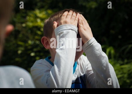 Boy hiding behind hands while playing hide and seek Stock Photo