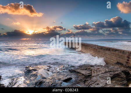 Beautiful golden sun rays as it sets over the stone pier at Porthleven on the Cornwall coast Stock Photo