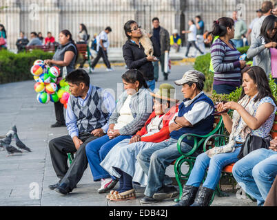 Local people including an old lady in traditional dress wearing a hat sitting on benches in the popular crowded Plaza de Armas, Arequipa, Peru Stock Photo