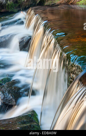 A small moorland stream cascading over a weir captured using a slow shutter speed to blur the movement of the water. Stock Photo