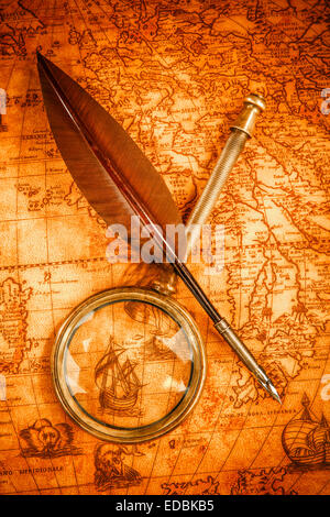 Vintage magnifying glass and quill pen on an old ancient map in 1565. Vintage still life. Stock Photo