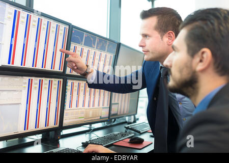 Businessmen trading stocks. Stock traders looking at graphs, indexes and numbers on multiple computer screens. Colleagues in dis Stock Photo