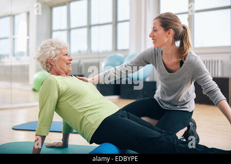 Physical therapist working with a senior woman at rehab. Female trainer helping senior woman doing exercise on foam roller at gy Stock Photo