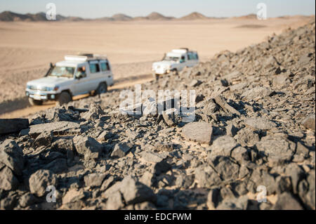 Two off road vehicles driving through a desolate arid rocky desert landscape Stock Photo