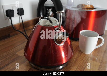 Kettle boiling with steam and toaster cooking toast behind in kitchen plugged in electrical appliances Stock Photo