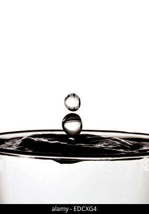 Water drop collision into a glass of water.  Mono shot showing water droplets splashing creating unusual shapes. Stock Photo