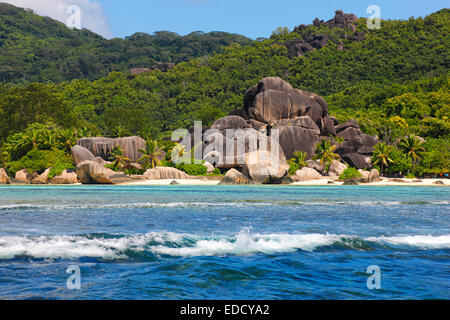 Big waves in front of granite rocks and a hill on island la Digue, Seychelles. Beach - Anse source d' Argent. Stock Photo