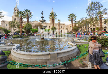 Local woman in traditional dress and hat resting against a fountain in Plaza de Armas, Arequipa, Peru Stock Photo