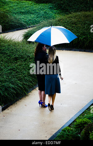 Two office girls standing outside under an umbrella in the rain and smoking cigarettes Stock Photo