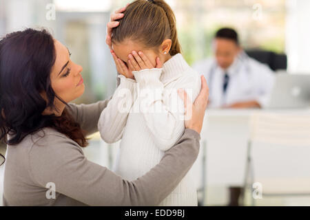 loving mother comforting her sick daughter in doctor's office Stock Photo
