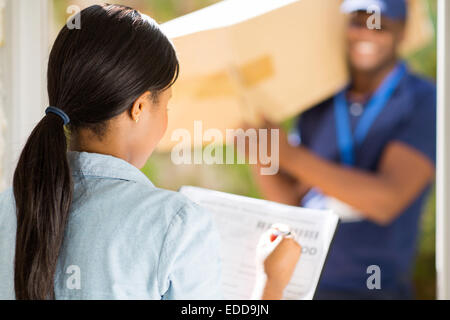 rear view African woman signing receiving paper from courier guy Stock Photo