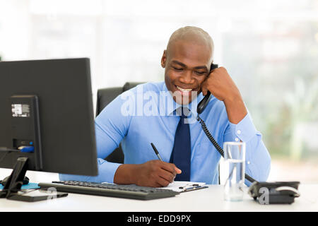 happy African businessman talking on landline phone and writing report Stock Photo