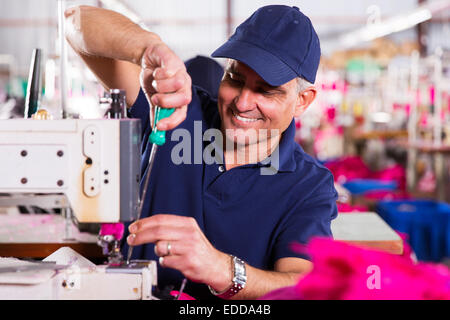 senior mechanic repairing industrial sewing machine in factory Stock Photo