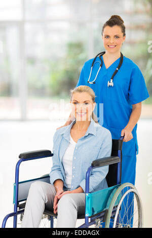 beautiful young nurse pushing middle aged patient on wheelchair Stock Photo