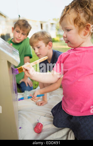 Three children in a garden, painting a dog house. Stock Photo