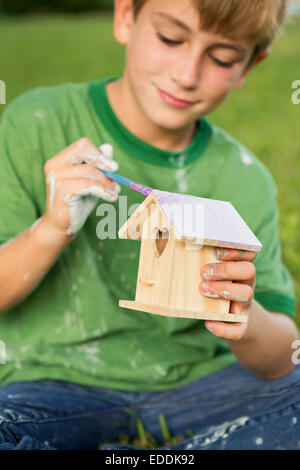 A boy in a garden, painting a bird house. Stock Photo