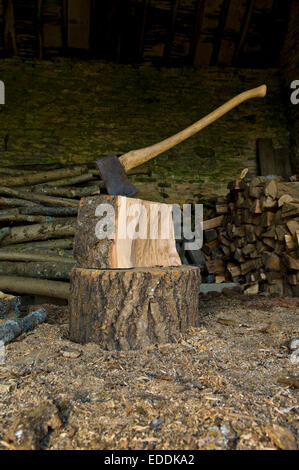 Axe stuck in a piece of wood on top of a chopping block, a pile of logs and chopped wood. Stock Photo