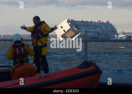 Cowes, Isle of Wight. 6th January, 2015. Life goes on in The Solent. Inshore RNLI Lifeboat stands by. Capsized car carrier Hoegh Osaka in the late afternoon sunshine. Surveyors and survey ships are in attendance to assess the state of the ship and its cargo. Windy weather is expected in the next few days. Credit:  Patrick Eden/Alamy Live News Stock Photo