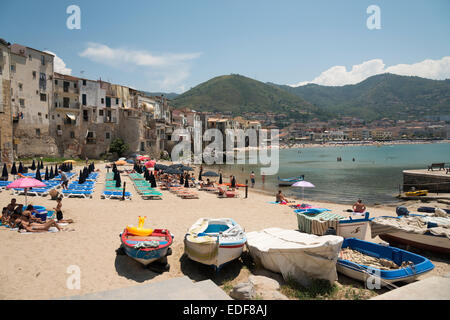 People and boats on the beach at the old port and old town at Cefalu Sicily Italy with ancient old buildings in the background. Stock Photo