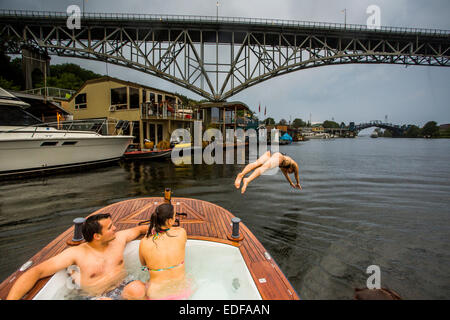 A young woman dives off the bow of a hot tub boat in Lake Union during a rain storm. Stock Photo