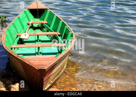 Red-green colored wooden rowboat chained to a stake on the shore of the 4.43 km2-784 ms.high Phewa tal-lake. Pokhara. Stock Photo