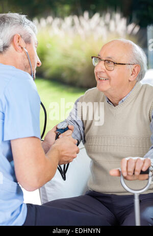 Male Doctor Measuring Blood Pressure Of Elderly Man Stock Photo