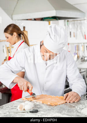 Chef Cutting Ravioli Pasta At Counter In Kitchen Stock Photo