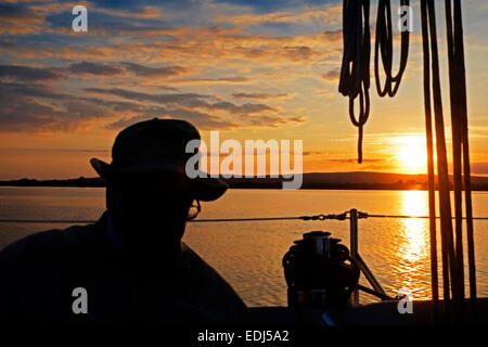 Man relaxing while Sailing at Sunset on a placid lake in Ireland. Stock Photo