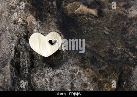 A bright beautiful metal heart is placed on a dark wet rock on a beach. Stock Photo